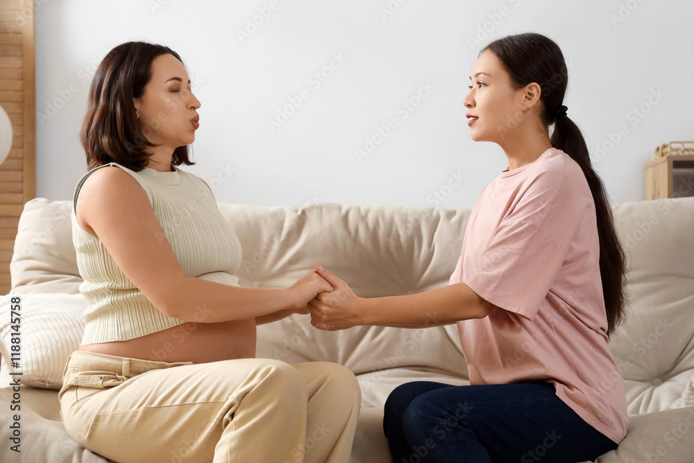 Young Asian doula with pregnant woman holding hands on sofa at home Young Asian doula with pregnant woman holding hands on sofa at home