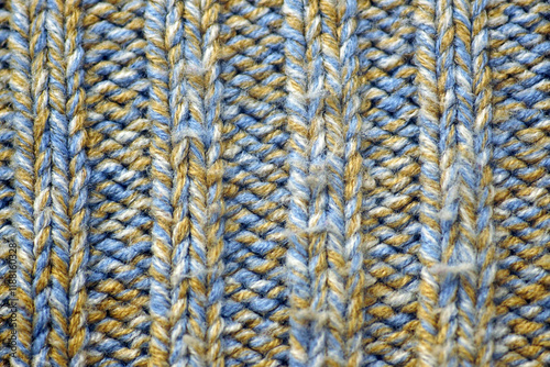 A product knitted using two different techniques from natural multi-colored yarn. Blue and yellow sweater with a combination of stockinette stitch and purl stitch close-up. Cozy background.