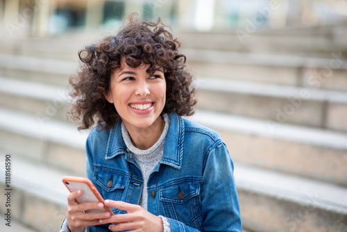 Smiling woman wearing denim jacket holding phone outdoors