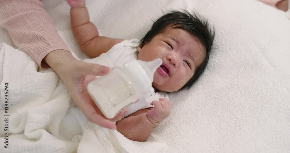Mother feeding newborn baby with milk bottle while lying on soft white blanket. Represents warmth, nourishment, love, and an intimate connection during early parenting and caregiving moments.