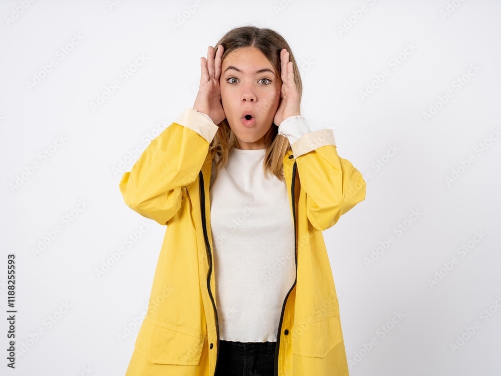 Beautiful teen girl wearing rain coat with scared expression, keeps hands on head, jaw dropped, has terrific expression. Omg concept Beautiful teen girl wearing rain coat with scared expression, keeps hands on head, jaw dropped, has terrific expression. Omg concept