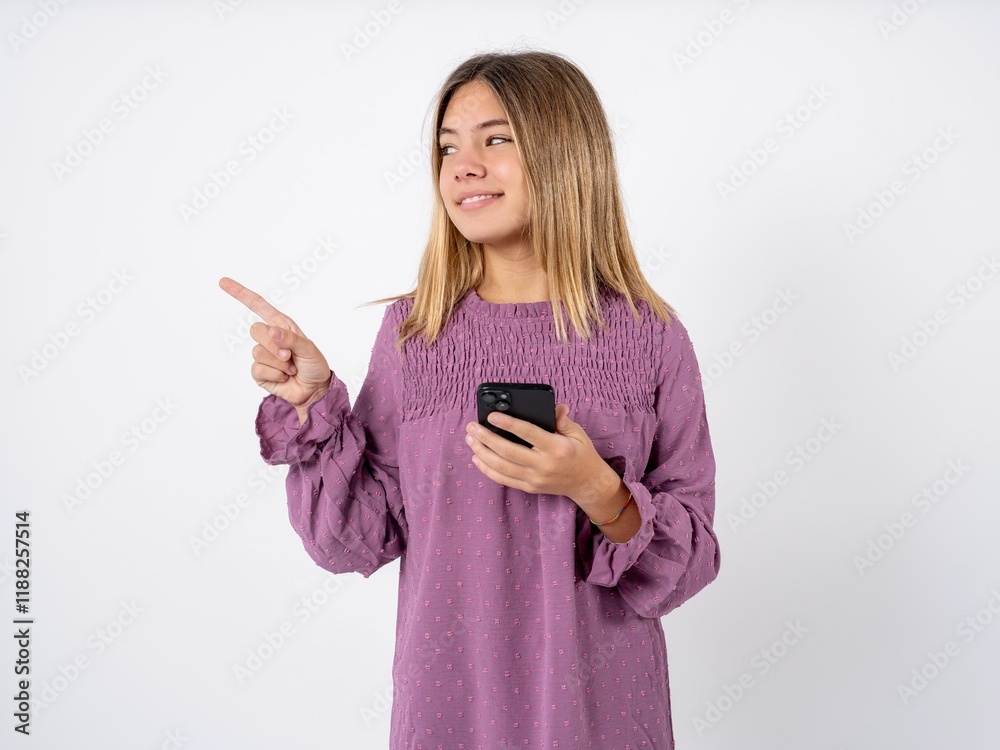 Smiling Beutiful caucasian gteen girl wearing pink T-shirt holding mobile phone and pointing aside at copyspace. Smiling Beutiful caucasian gteen girl wearing pink T-shirt holding mobile phone and pointing aside at copyspace.