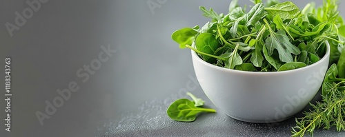 A minimalist scene with a white bowl filled with fresh greens like spinach, arugula, and herbs, set on a smooth grey surface with gentle studio lighting.  photo