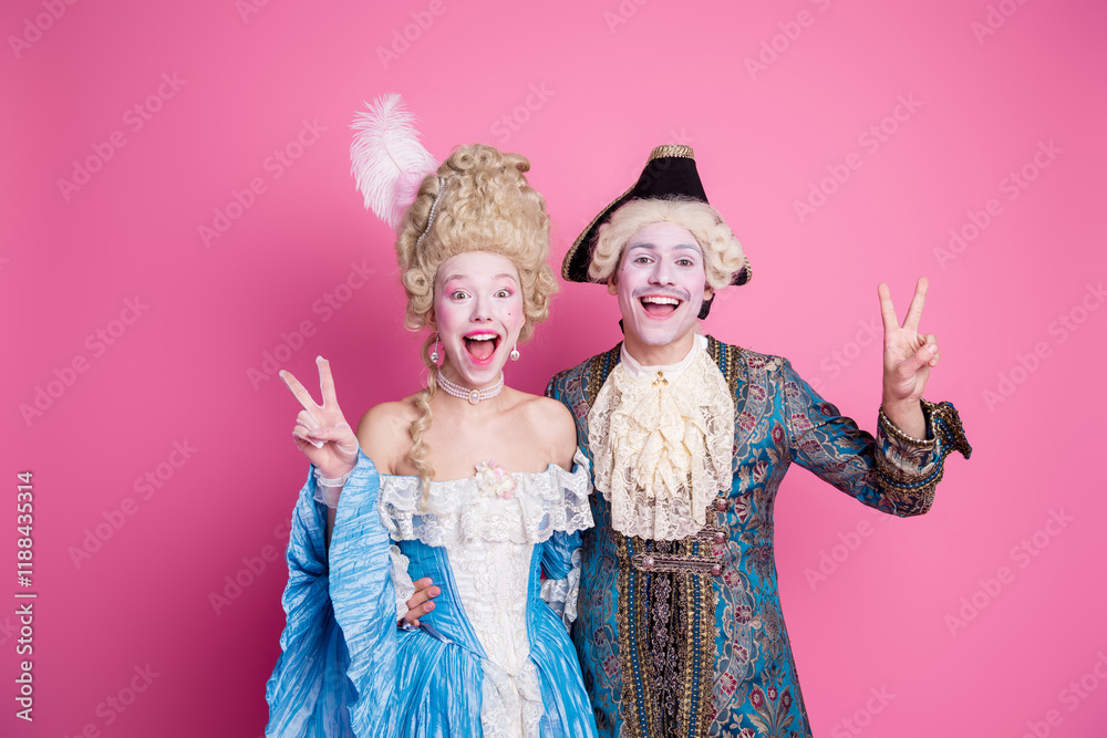 Fototapeta premium Two young adults in vibrant baroque costumes pose joyfully against a pink backdrop, embodying elegance and fun.