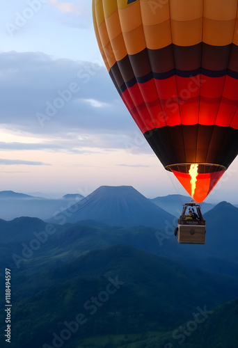 A hot air balloon drifts above vibrant green mountains with a volcano in the soft light of dawn.
