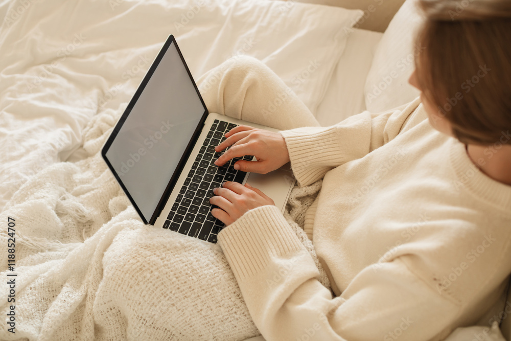 Overhead view of a young woman in casual loungewear sitting on her bed working on her laptop computer Overhead view of a young woman in casual loungewear sitting on her bed working on her laptop computer
