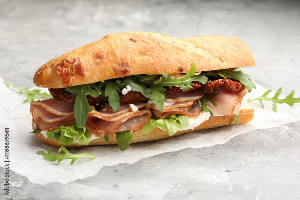 Obraz premium Baguette sandwich with ham and sun dried tomatoes on grey textured table, closeup