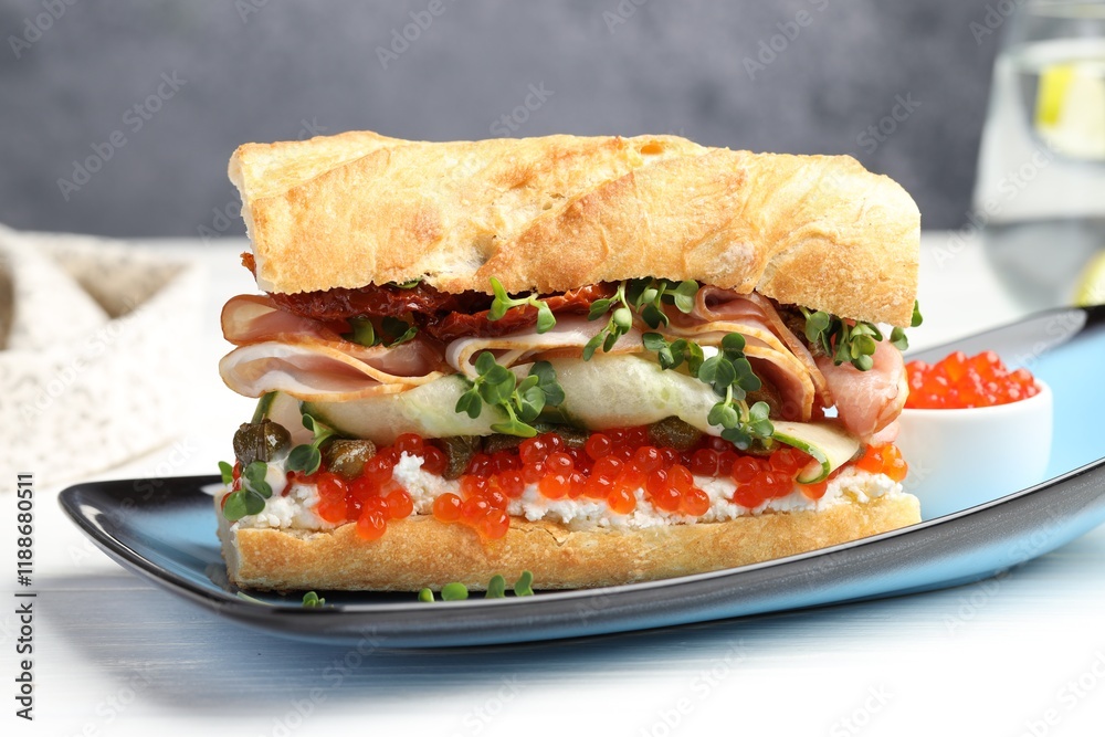Delicious baguette sandwich with caviar, ham and capers on white wooden table, closeup