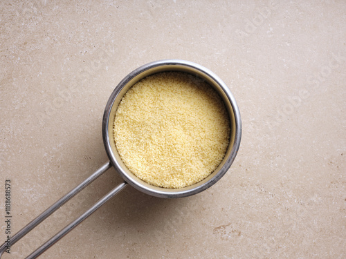 Preparing a traditional Mediterranean dish, fine couscous is shown in a metal measuring cup, ready to be combined with fresh herbs, vegetables, and spices for a tasty tabbouleh. photo