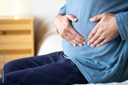 Man sitting alone on his bed and suffering from stomach cramps while home alone.Abdominal pain can be caused by digestive problems, infections, intestinal inflammation or more serious diseases. photo