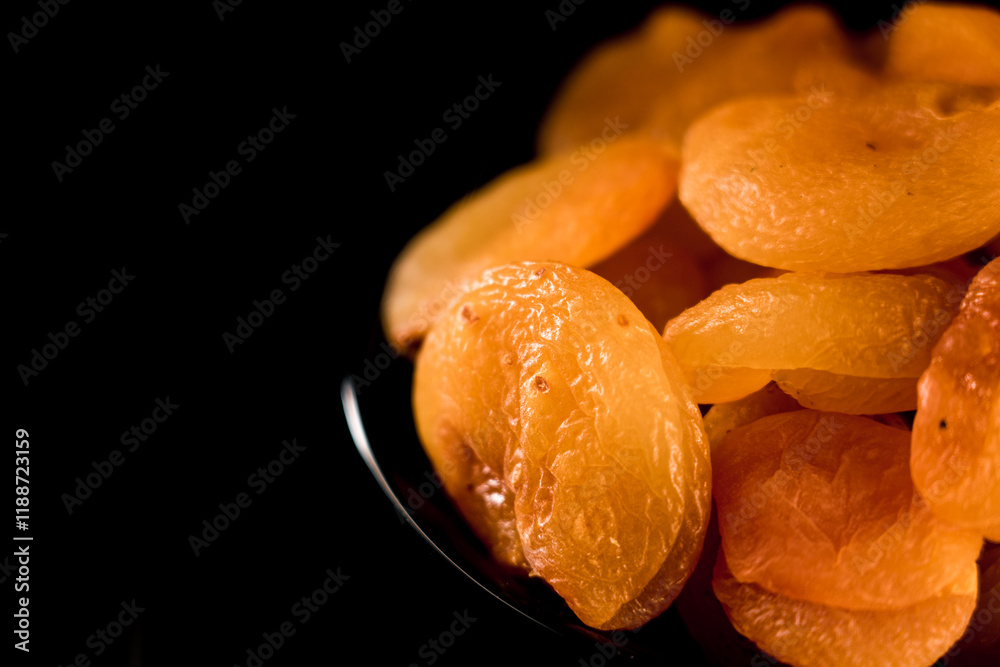 Dried apricots piled on a plate showcasing rich texture against a vivid black background Dried apricots piled on a plate showcasing rich texture against a vivid black background