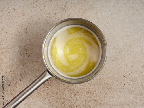 A close-up view captures melted butter and warm milk combining in a stainless steel pot. The swirl pattern creates a creamy texture, reflecting a cozy kitchen vibe