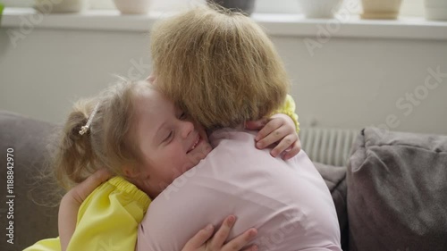 Smiling child with Down syndrome hugs her mother in warm, inviting home. Interaction highlights nurturing of emotional and psychological health. Concept: well-being, psychological support, family love