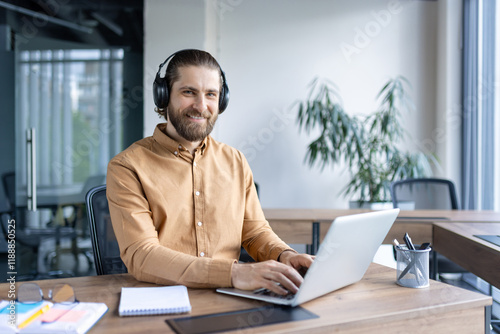 Smiling professional wearing headphones operates a laptop in a bright, modern workspace. photo