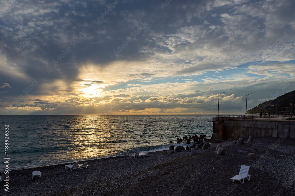 Dramatic sky with dark clouds on calm sea at sunset. Black Sea coast, early autumn. Deserted beach. Beach loungers Dramatic sky with dark clouds on calm sea at sunset. Black Sea coast, early autumn. Deserted beach. Beach loungers