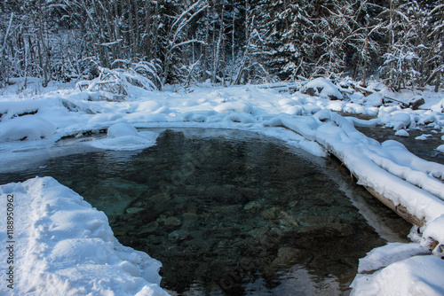 Clear, calm water in the backwaters of a mountain river. The shores are covered with white fluffy fresh snow. Winter landscape