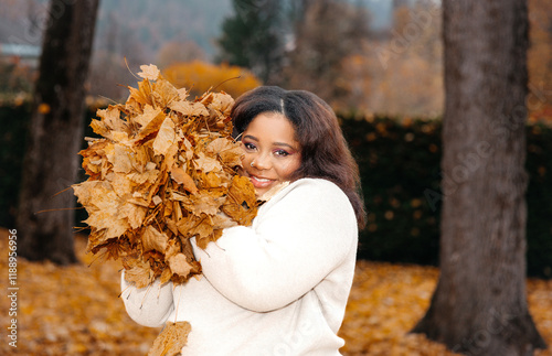 Konstfotografi African female smiling with autumn leaves in park