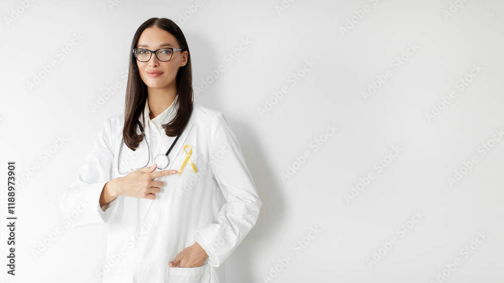 Childhood cancer awareness concept. Female doctor pointing at yellow ribbon on her lab coat, standing over white background, panorama, free space Childhood cancer awareness concept. Female doctor pointing at yellow ribbon on her lab coat, standing over white background, panorama, free space