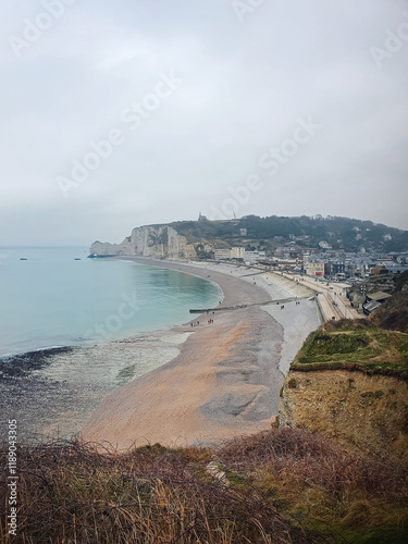 Coastal town Etretat with a pebble beach, cliffs, and a calm sea. The famous Falaise d'Aval cliffs in Normandy, France