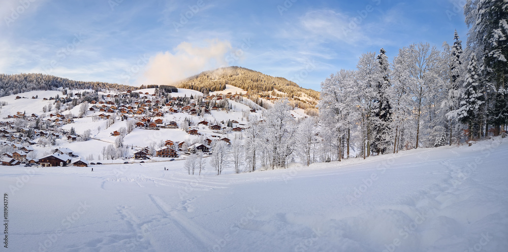 Winter panorama of snow covered La Clusaz village nestled in a hilly landscape in Annecy, France. Wooden cabins are scattered across the snowy hillside, surrounded by snow laden trees