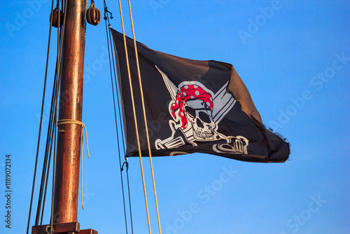Obraz na płótnie The pirate flag or the Jolly Roger - old shabby black flag with a skull waving on the mast of a sailing ship w salonie