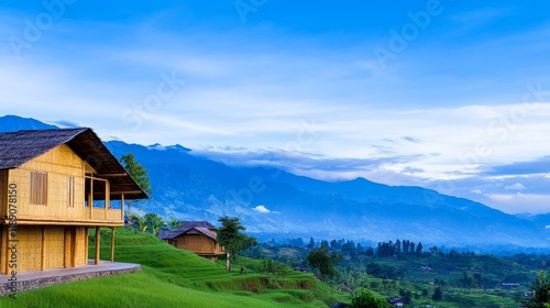 Scenic view of bamboo houses on a hillside with mountain and blue sky in the background.