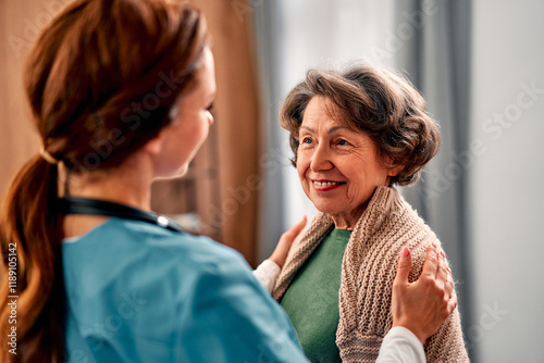 A modern senior woman looks at the doctor with a smile and gratitude for his care. The nurse expresses support with a gesture of placing her hands on the woman's shoulders.Elder care.
