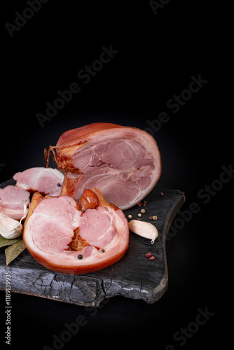 Appetizing smoked pork shank sliced , on a charred chopping board isolated on black background photo