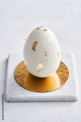 A golden egg with decorative leaf accents sits atop a circular marble pedestal. The contrast between the smooth egg and the textured base creates an elegant display fitting for a luxurious setting photo