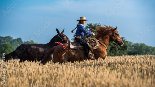 Cowgirl riding her horse and leading a mule in a wheat field.