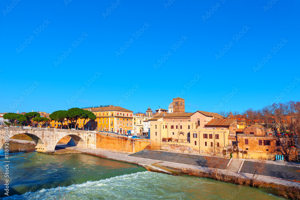Picturesque view of historic bridge and buildings along Tiber river in Rome. Blue sky, flowing river, and charming architecture make scene visually appealing and indicative of culturally rich location