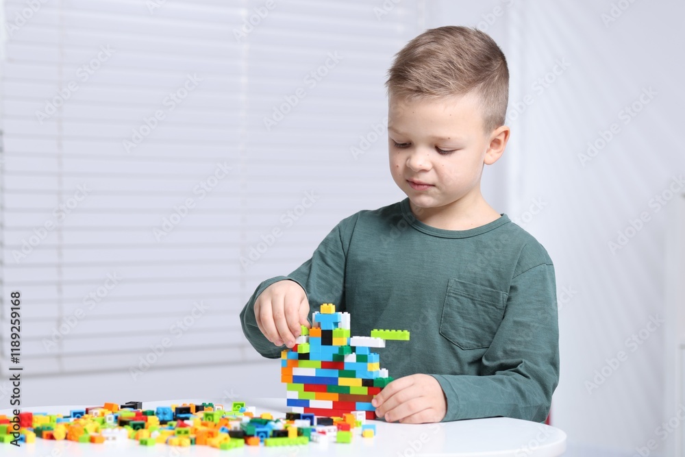 Cute boy playing with building blocks at white table indoors. Space for text Cute boy playing with building blocks at white table indoors. Space for text