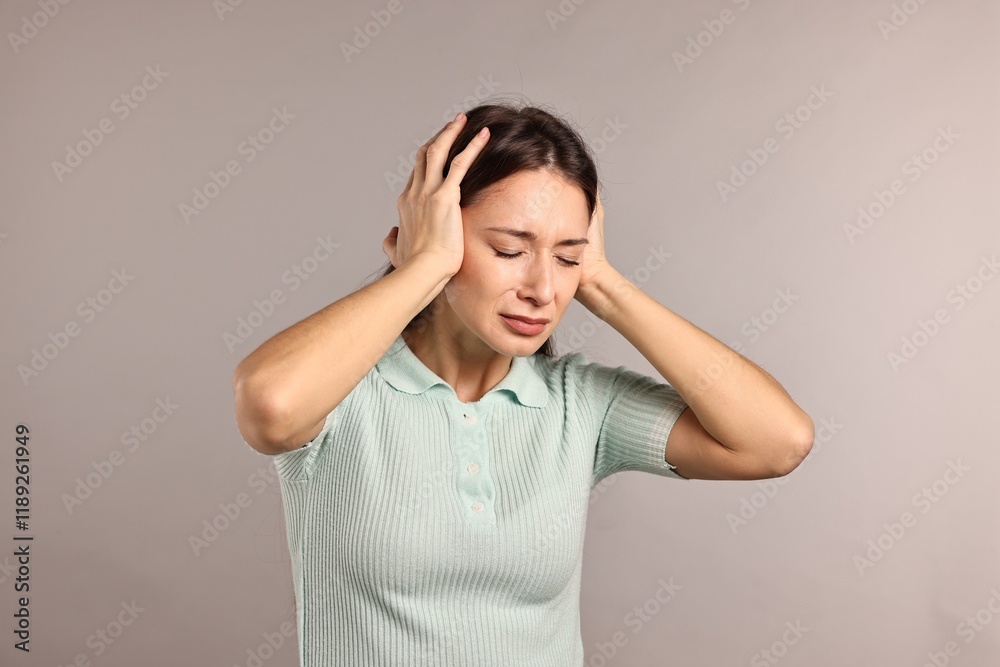 Annoyed woman covering her ears due to loud sound on light grey background Annoyed woman covering her ears due to loud sound on light grey background