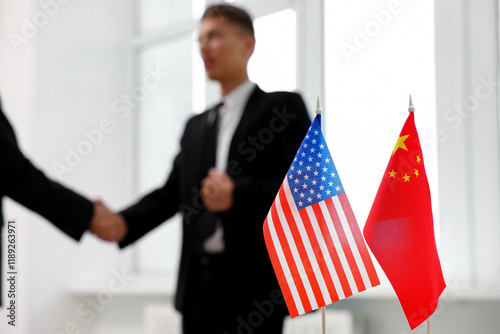 Diplomats shaking hands during meeting indoors, focus on flags of USA and China photo
