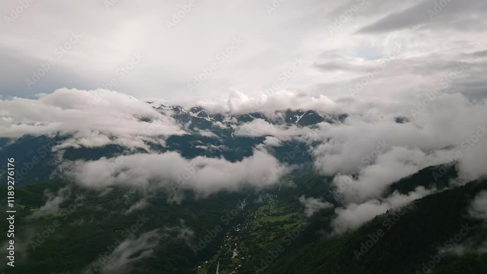 Aerial view of Mazeri village mountains in Svaneti with clouds drifting. Lush green forests, snow-capped peaks contrast with clouds. Tranquil nature scene, remote mountain landscape. Drone shot Aerial view of Mazeri village mountains in Svaneti with clouds drifting. Lush green forests, snow-capped peaks contrast with clouds. Tranquil nature scene, remote mountain landscape. Drone shot