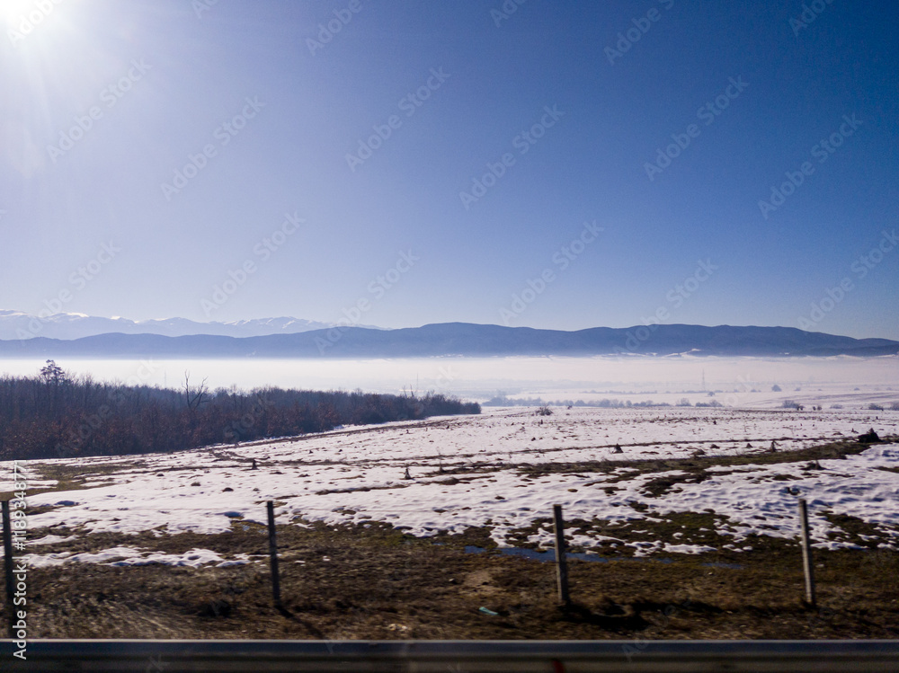 View to field and mountain with fog and snow from highway