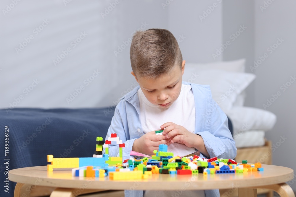 Cute boy playing with building blocks at wooden table indoors Cute boy playing with building blocks at wooden table indoors