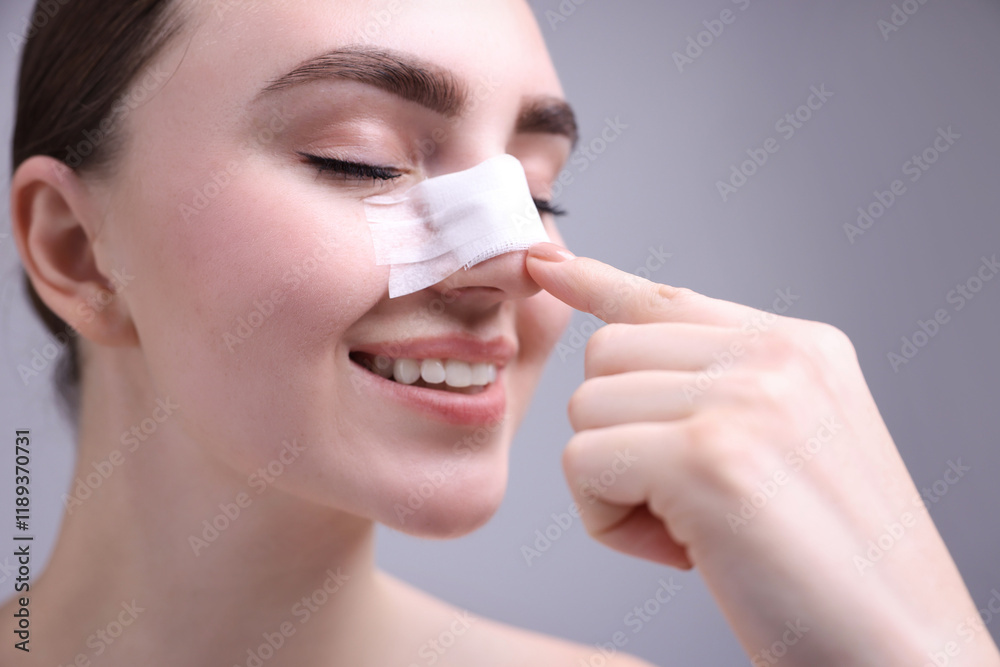 Woman with medical bandage on her nose after plastic surgery operation against grey background