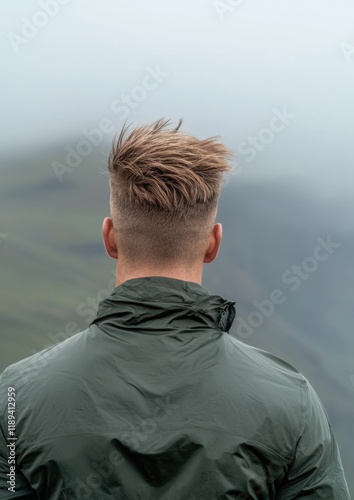 The back of a man's head and upper body, facing away from the camera. he is wearing a dark green jacket with a hood. the man's hair is styled in a short, spiky cut with a side part. photo