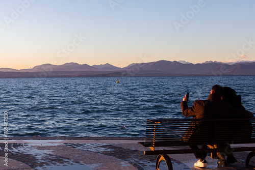 Obraz na płótnie Lazise: couple takes photos at sunset on Lake Garda. w salonie