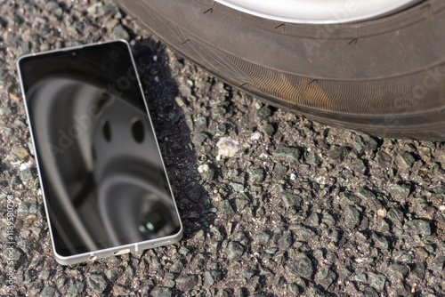車のタイヤの横に落ちたスマートフォン