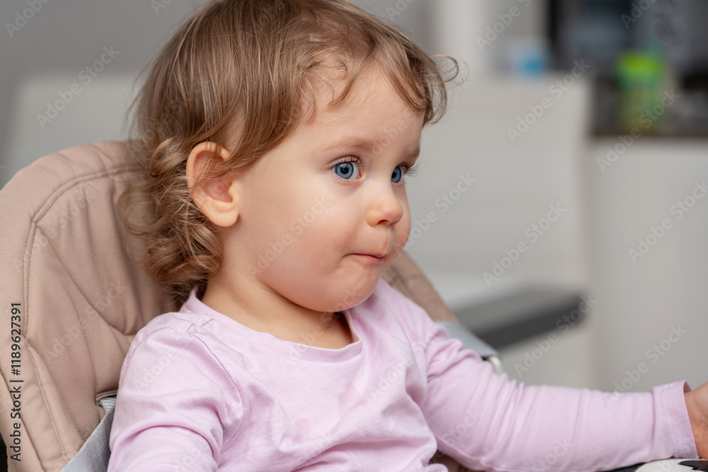 A thoughtful toddler seated in a highchair observing their surroundings with quiet curiosity. A thoughtful toddler seated in a highchair observing their surroundings with quiet curiosity.