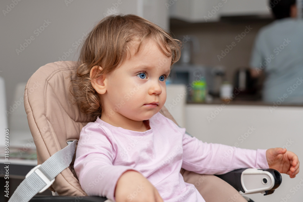 A calm toddler seated in a highchair observing the home surroundings with curiosity. A calm toddler seated in a highchair observing the home surroundings with curiosity.