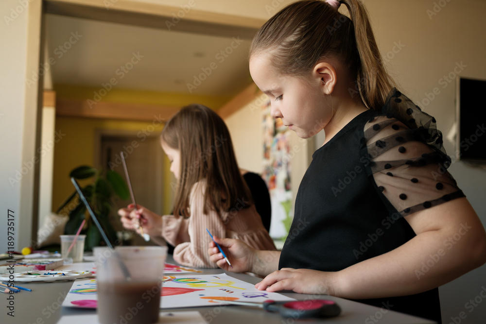 Two young girls attentively painting at a table, concentrating on their artistic creations with colorful materials. Two young girls attentively painting at a table, concentrating on their artistic creations with colorful materials.