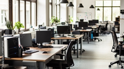 A clean and organized office workspace featuring rows of desks with PC desktops, complemented by large windows allowing natural light. photo