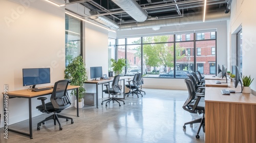 A modern office coworking space featuring PC monitors on tables, a large window, and an empty wall, designed to foster productivity and collaboration. photo