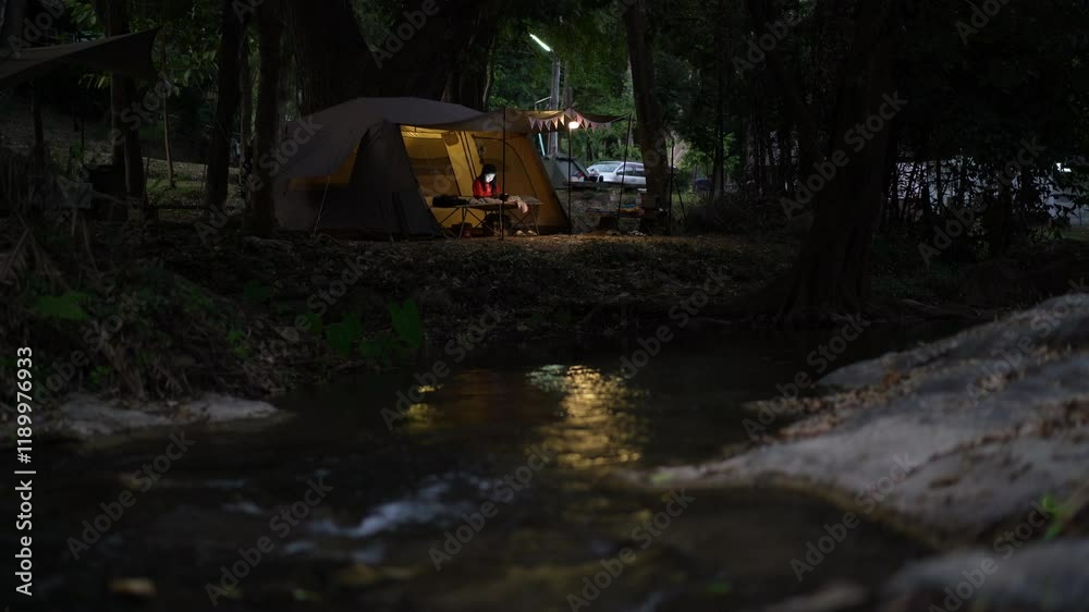 nature camping and camper relaxing in front of tent with warm white lamp on twilight and water stream at garden forest lan sang waterfall national park campground on holiday vacation with stream sound nature camping and camper relaxing in front of tent with warm white lamp on twilight and water stream at garden forest lan sang waterfall national park campground on holiday vacation with stream sound