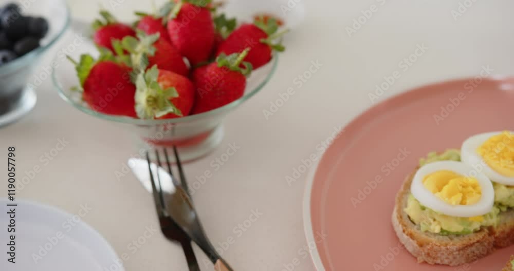 Fresh strawberries in glass bowl with blueberries and cutlery on table, at home Fresh strawberries in glass bowl with blueberries and cutlery on table, at home