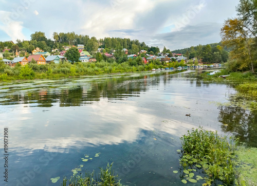 Village lake with houses and boats on the shore, banks overgrown with reeds, summer rural calm landscape photo