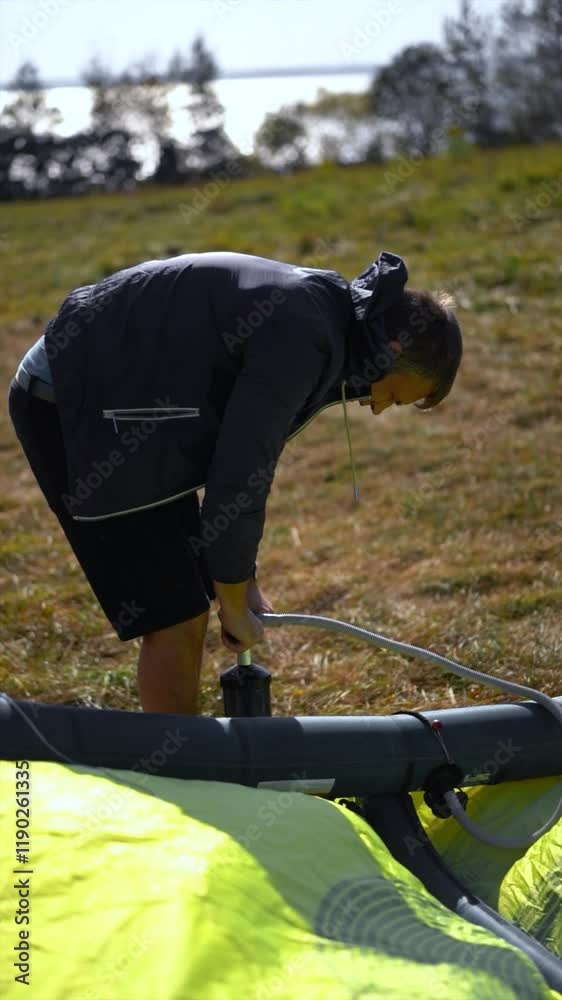A man in wetsuit pumps up a kiteboarding kite on a beach